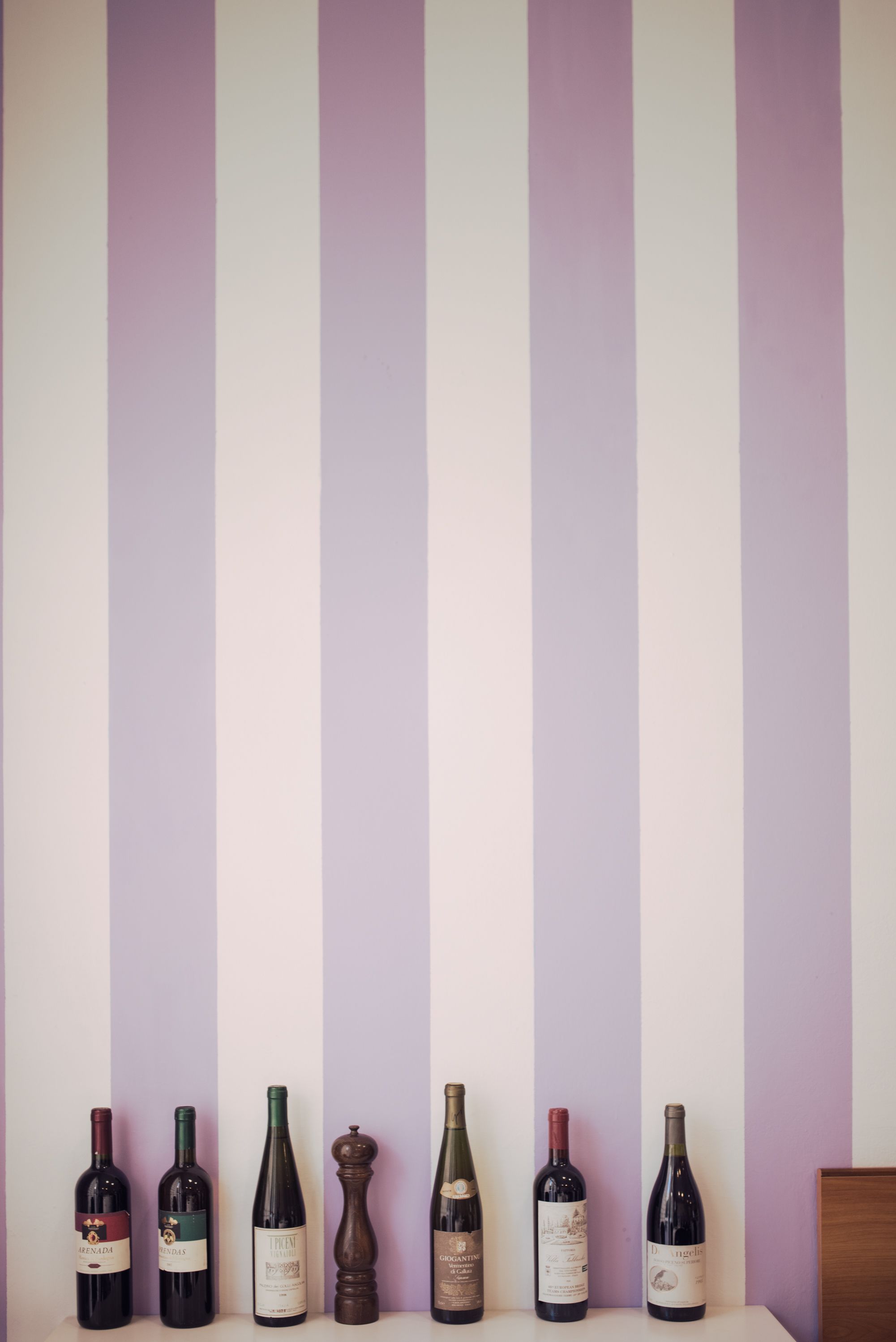 Seven wine bottles aligned against a striped wall.