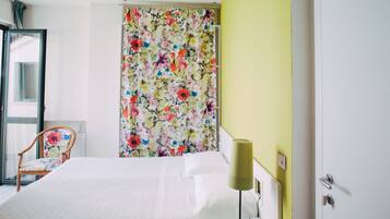 A hotel room with a bed, a chair, a curtain with a floral pattern, and a lamp.