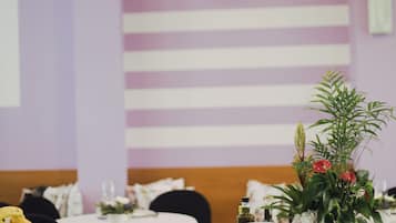 Un comedor con mesas dispuestas para una comida, con platos apilados y un centro de mesa con plantas.