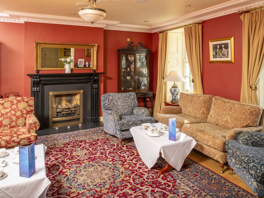 Ein traditionell eingerichtetes Zimmer mit Kamin, gemusterten Sofas und einem roten Teppich.
