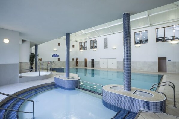 An indoor swimming pool with clear water, tiled walls, and a central column.