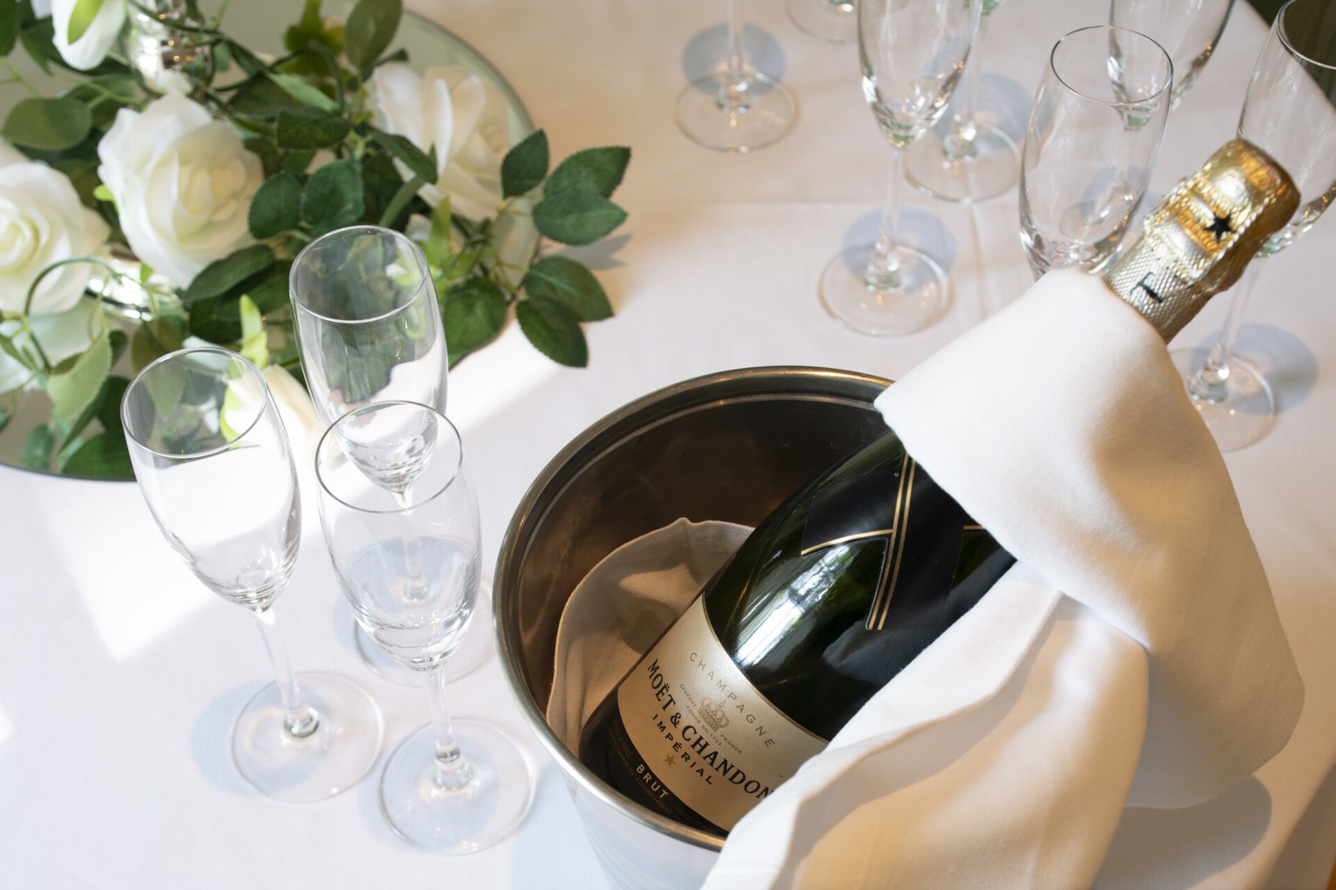 A champagne bottle in a metal bucket with a white cloth, surrounded by empty wine glasses on a table.