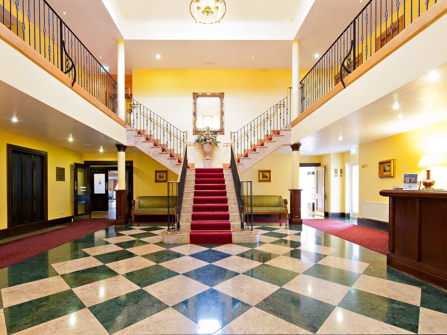 Eine prachtvolle Lobby mit Schachbrettmuster-Boden, einer zentralen Treppe und einem Kronleuchter.