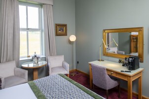 Habitación de hotel con cama, escritorio, silla, una mesita con un cubo de copas de champán, lámpara de pie y un espejo grande.