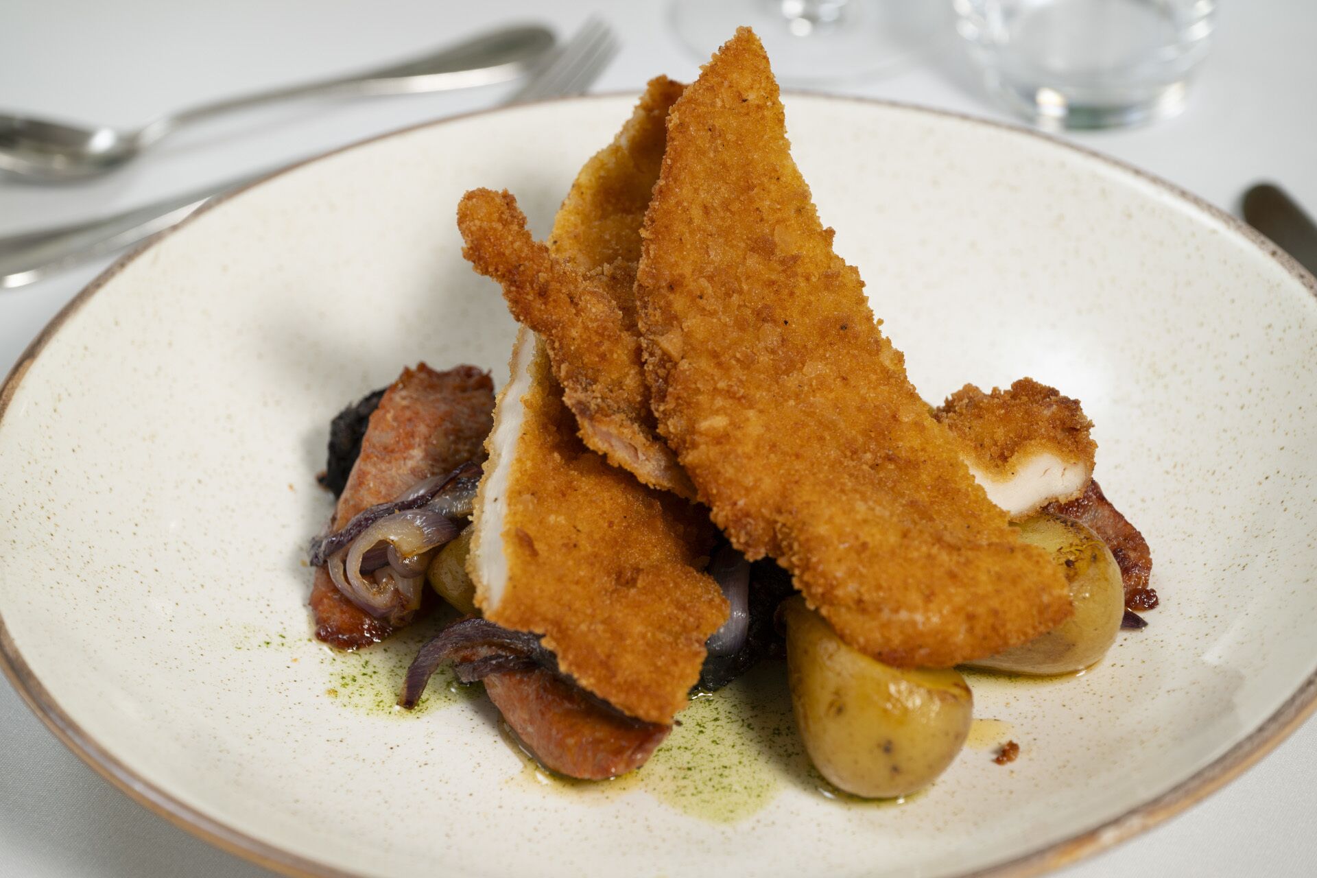 A plate with breaded fish fillets, potatoes, and onions.