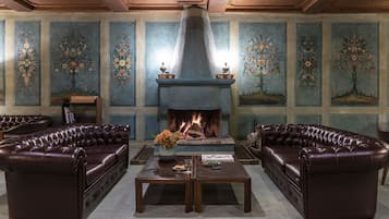 Una habitación con chimenea, sofás de cuero, una mesita de café y decoración floral en las paredes.