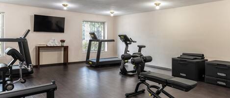 A gym with exercise equipment, a television, and a window with blinds.