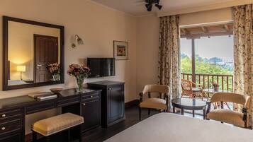 A hotel room with a bed, a desk with a lamp, a television, and two chairs.