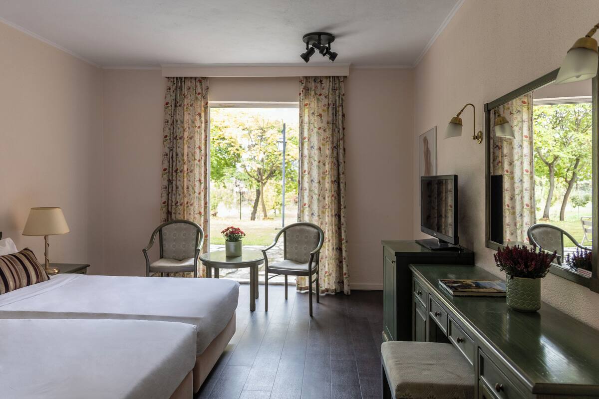 Ein Hotelzimmer mit zwei Betten, einem Schreibtisch mit Stuhl, einem Fernseher und Blick ins Freie.