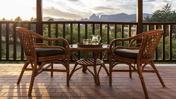 Een houten terras met rieten stoelen en een tafel, uitkijkend op een bergachtig landschap.