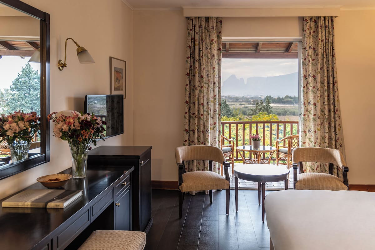 Ein Hotelzimmer mit einem Bett, einem Schreibtisch mit Computer, einem Sessel, einem kleinen Tisch und Blick auf Berge durch das Fenster.