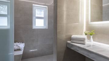 A modern bathroom with a large mirror, a window, and a marble countertop with towels.