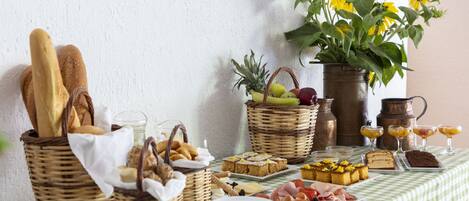 A breakfast buffet with bread, pastries, fruits, and beverages on a checkered tablecloth.