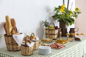 Een ontbijtbuffet met brood, gebak, fruit en drankjes op een geruit tafelkleed.