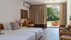 Quarto de hotel com duas camas, uma mesa, uma cadeira, um abajur e vista para o exterior.