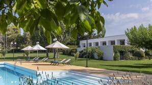 Piscina com espreguiçadeiras e guarda-sóis, rodeada por relvados bem cuidados e um edifício moderno.