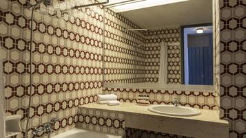 Ein Badezimmer mit Wandfliesen in Sechseckmuster, einem weißen Waschbecken, einem Spiegel und einer Duschkabine.