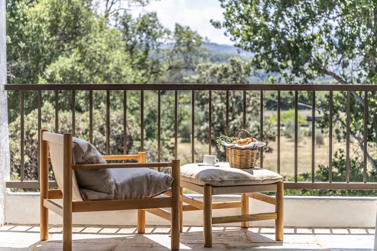 Un juego de mesa y silla de madera en un balcón con barandilla de metal, con vista a un paisaje natural.