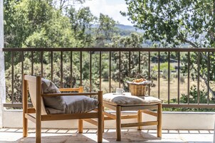 Un juego de mesa y silla de madera en un balcón con barandilla de metal, con vista a un paisaje natural.