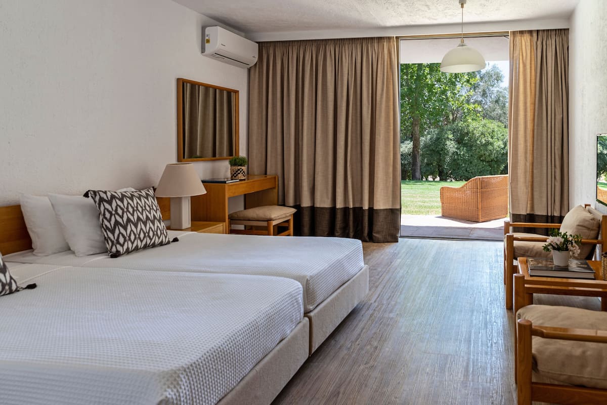 Habitación de hotel con dos camas, un escritorio, una silla, una lámpara y vistas al exterior.