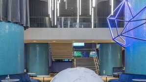 Un vestíbulo moderno con un gran globo como pieza central, una escalera y zonas de estar en tonos azules.