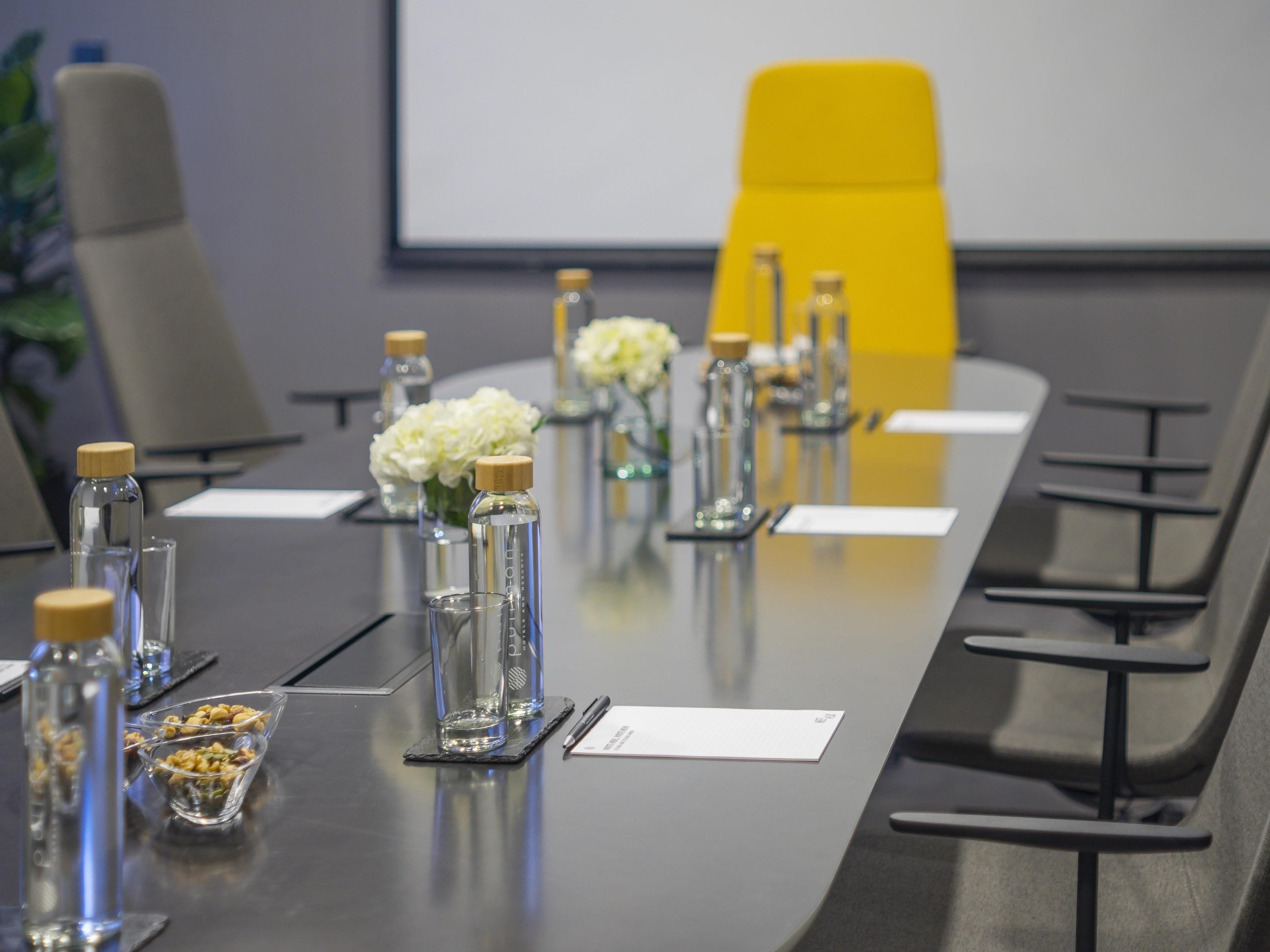 Una mesa de conferencias con botellas de vidrio, un cuenco de frutos secos y un arreglo floral blanco.