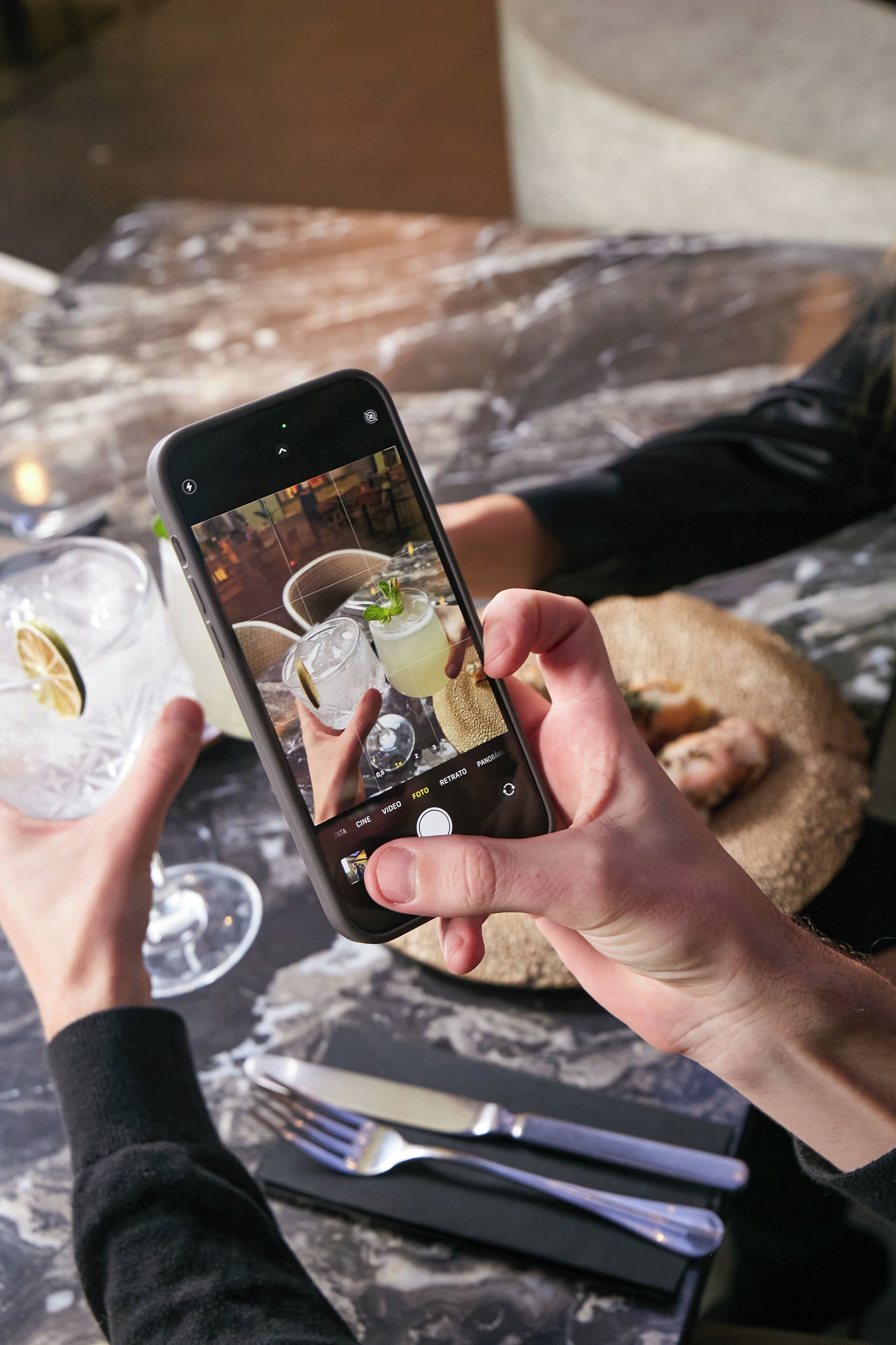 Una persona sostiene un teléfono inteligente que muestra una foto de una mesa con bebidas y una cesta de pan.