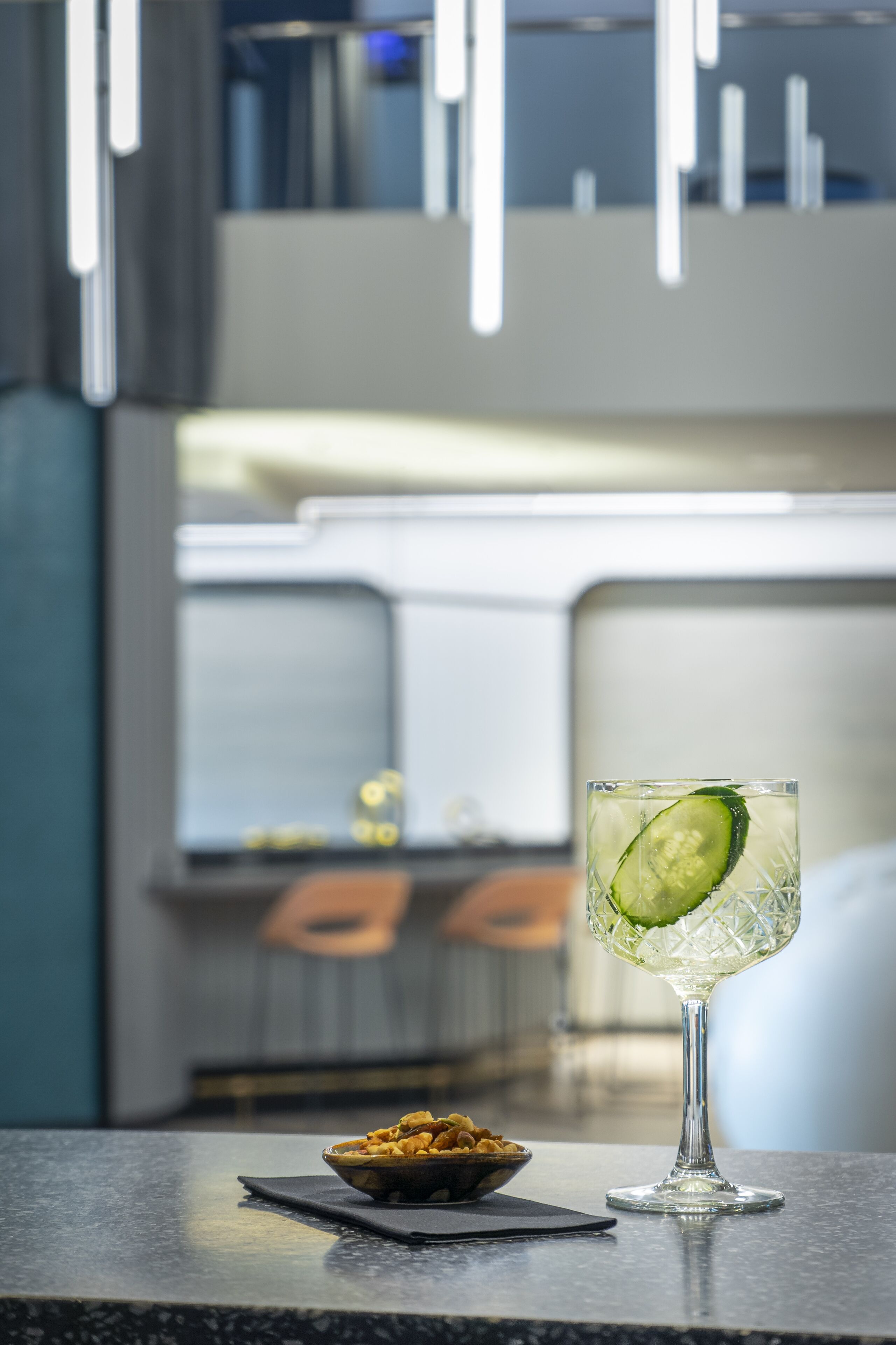 Una zona de bar con un vaso de cóctel de pepino, un cuenco de frutos secos y una decoración de estilo moderno.