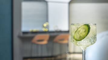 Una zona de bar con un vaso de cóctel de pepino, un cuenco de frutos secos y una decoración de estilo moderno.