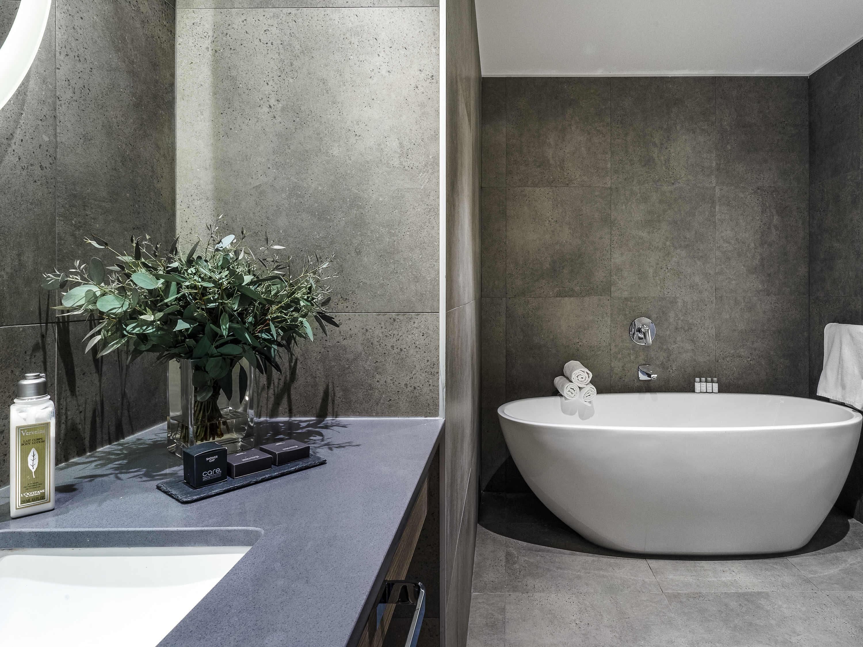 Un baño moderno con una bañera independiente, un espejo grande y una planta en el mueble de tocador.