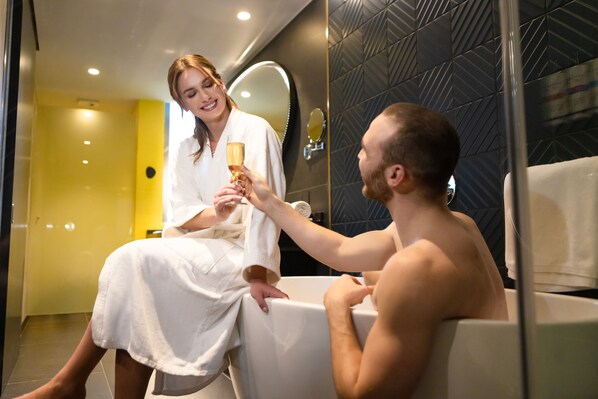 A man and a woman in a modern bathroom with a glass partition, a yellow wall, and a mirror. - Pullman Santiago El Bosque (Santiago)