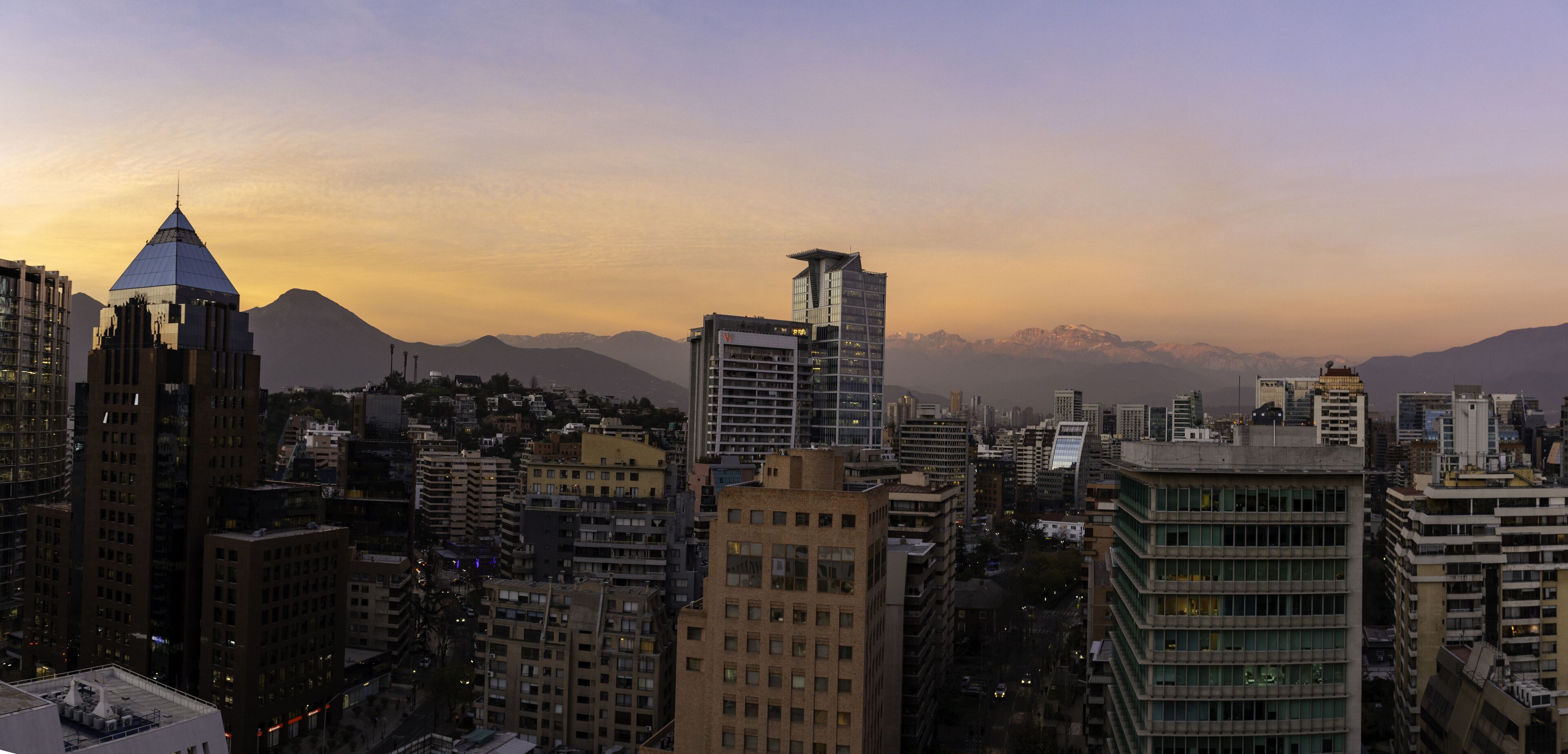 Un paisaje urbano con edificios modernos y una cadena montañosa al fondo.