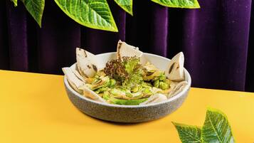 A bowl of salad on a yellow table with a purple curtain in the background.