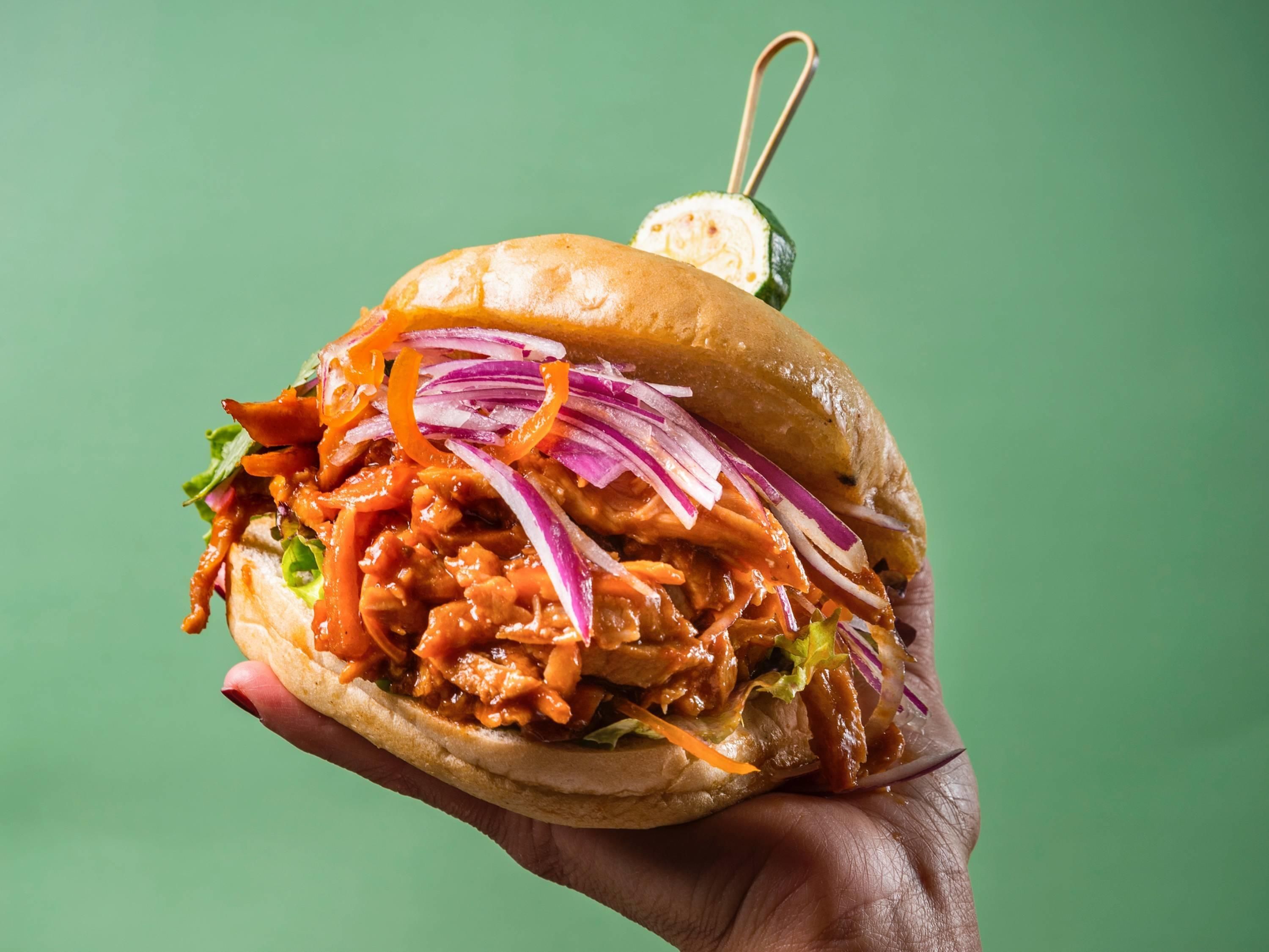 A hand holding a sandwich with visible lettuce, red onion, and a sauce.