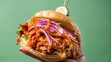 A hand holding a sandwich with visible lettuce, red onion, and a sauce.