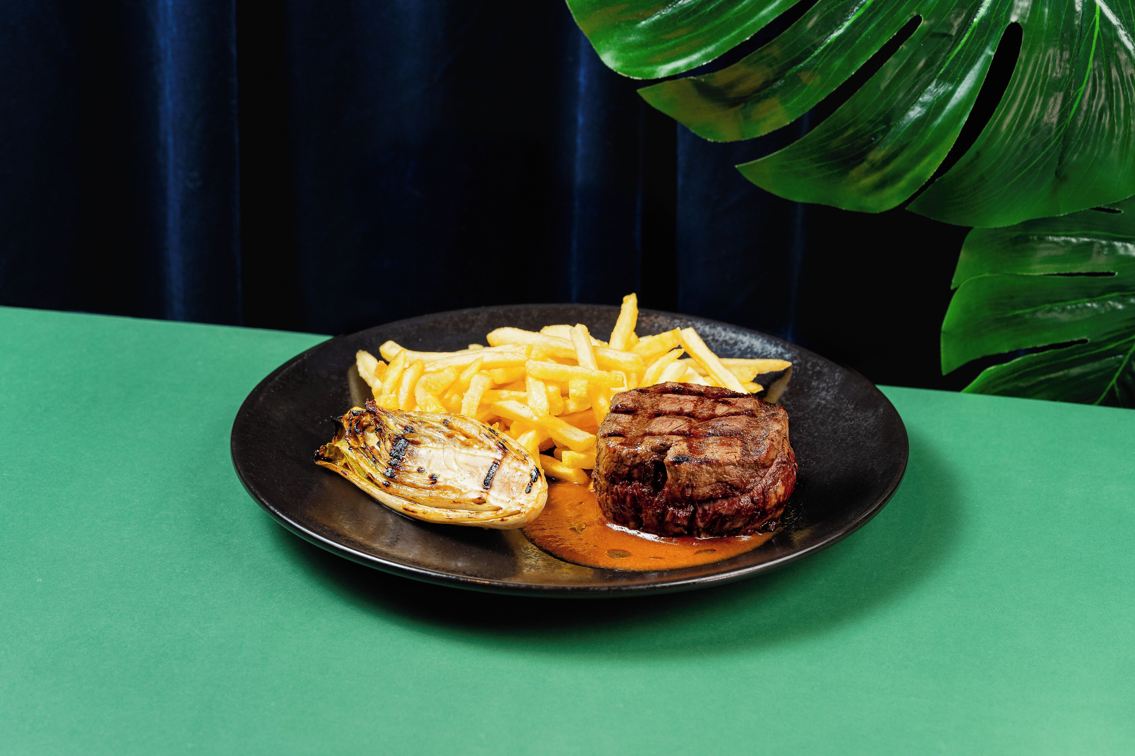 Une assiette contenant un steak grillé, des frites et un légume grillé, le tout présenté sur une assiette foncée.