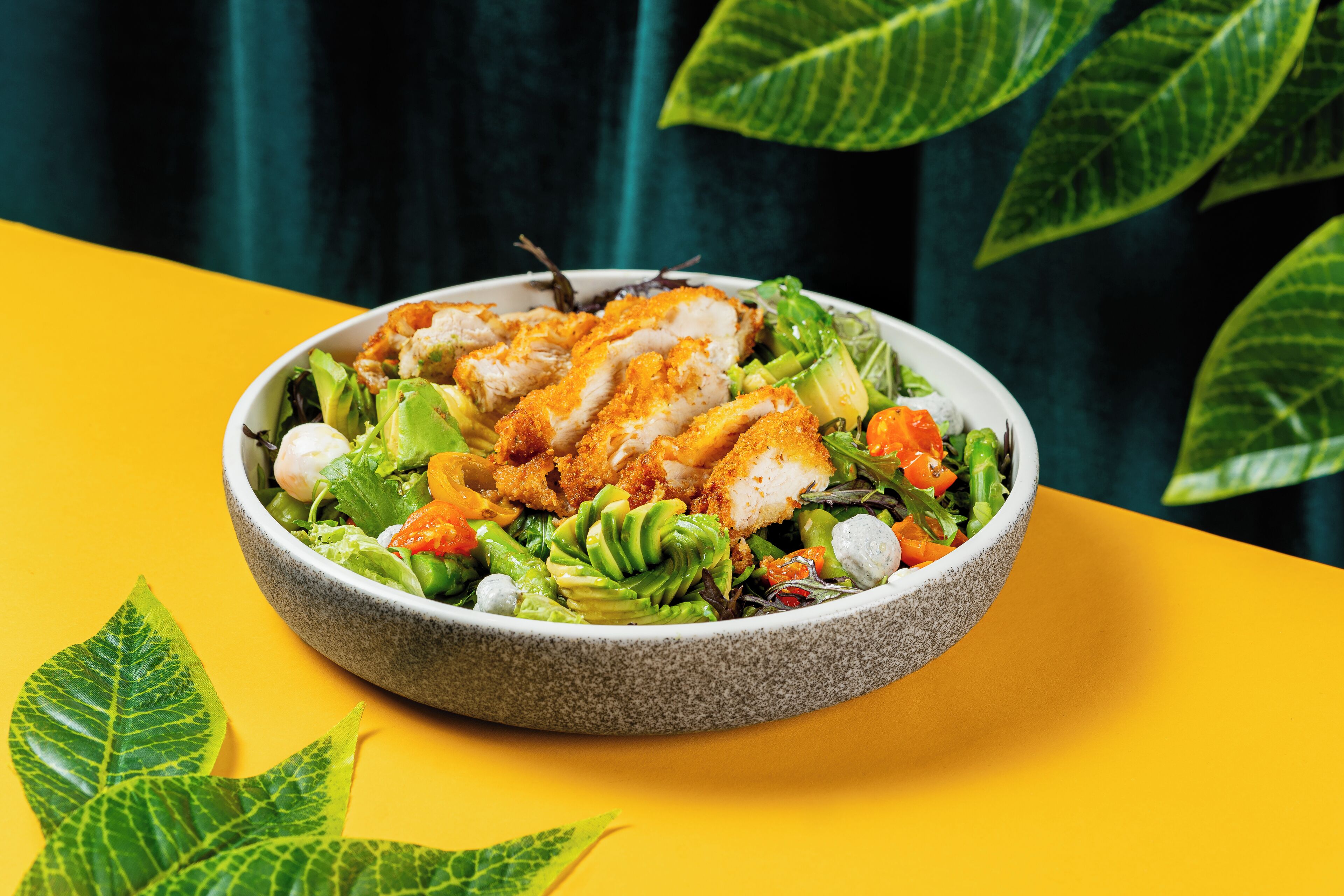 Eine Salatschüssel mit Hähnchen, Gemüse und einem Blatt als Dekoration.