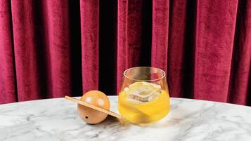 Un vaso de líquido amarillo con cubitos de hielo y una cuchara de madera sobre una mesa de mármol.