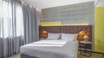 Een moderne hotelkamer met een groot bed, een rond bijzettafeltje met een vaas, en een hoofdeinde met wandlampen.