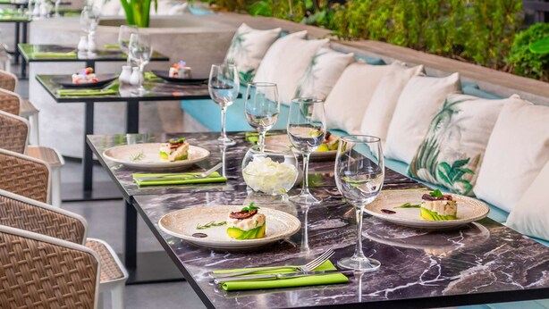 A restaurant with outdoor seating, green plants, and marble tables.