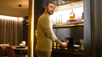 A man standing in a bar area with a well-lit shelf displaying bottles and glasses.
