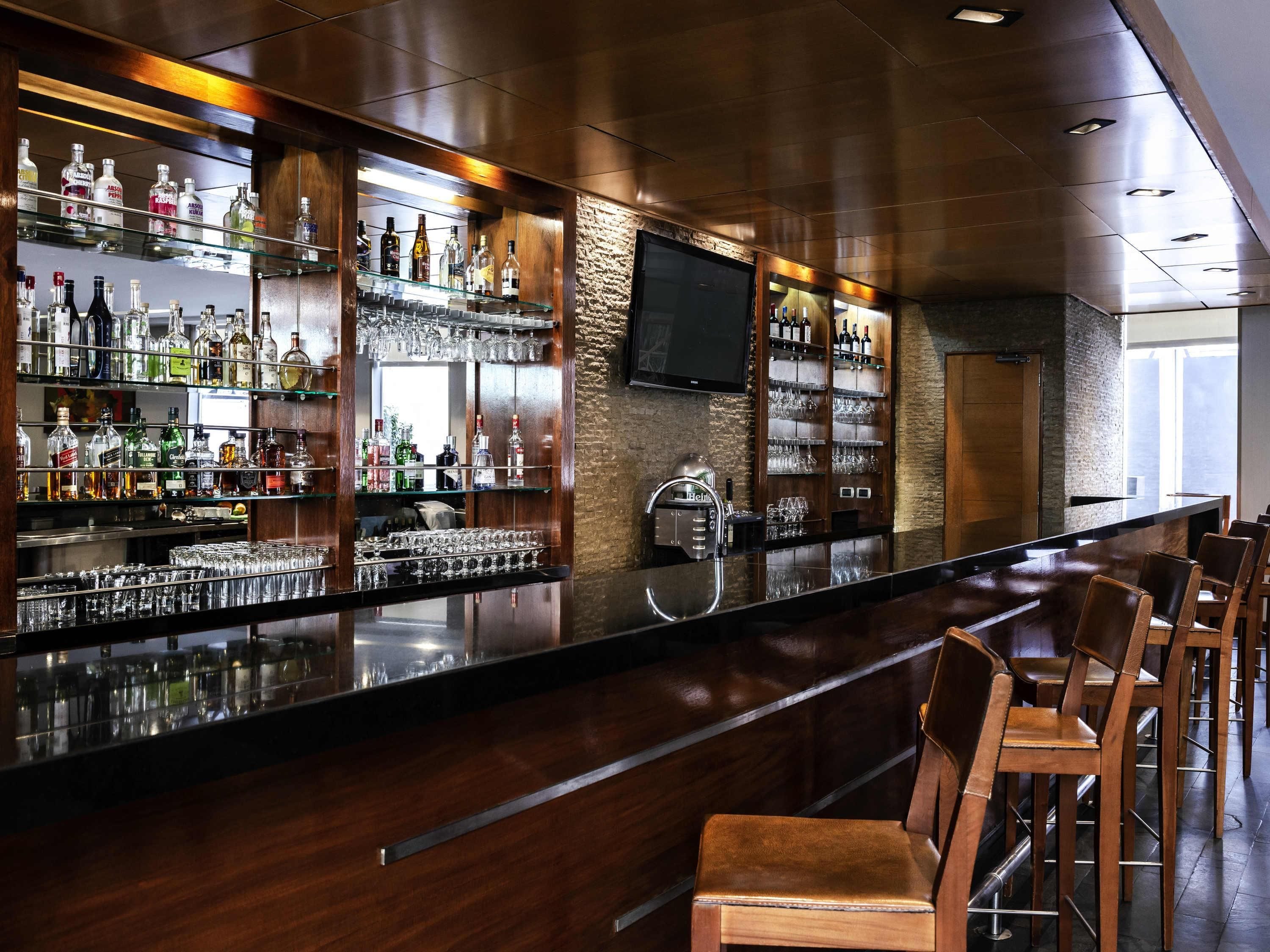 Un espace bar doté d’un long comptoir, de plusieurs étagères remplies de bouteilles d’alcool et d’un téléviseur fixé au mur.