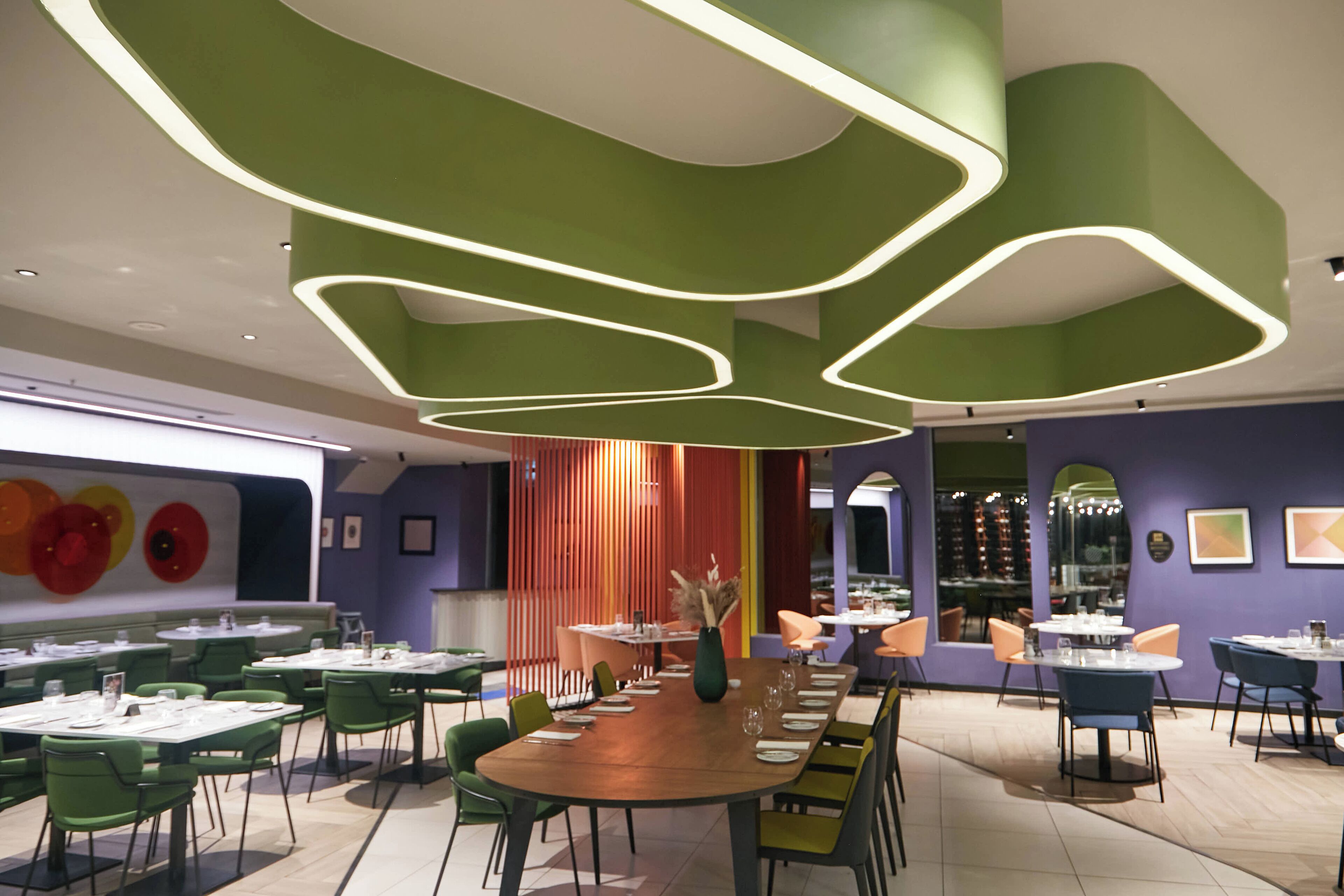 Un restaurante moderno con decoración verde y morada, varias mesas y sillas.
