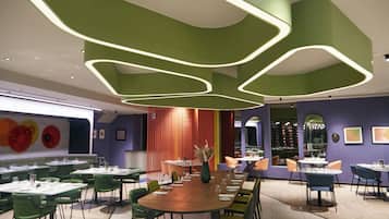 Ein modernes Restaurant mit grüner und violetter Einrichtung, mehreren Tischen und Stühlen.