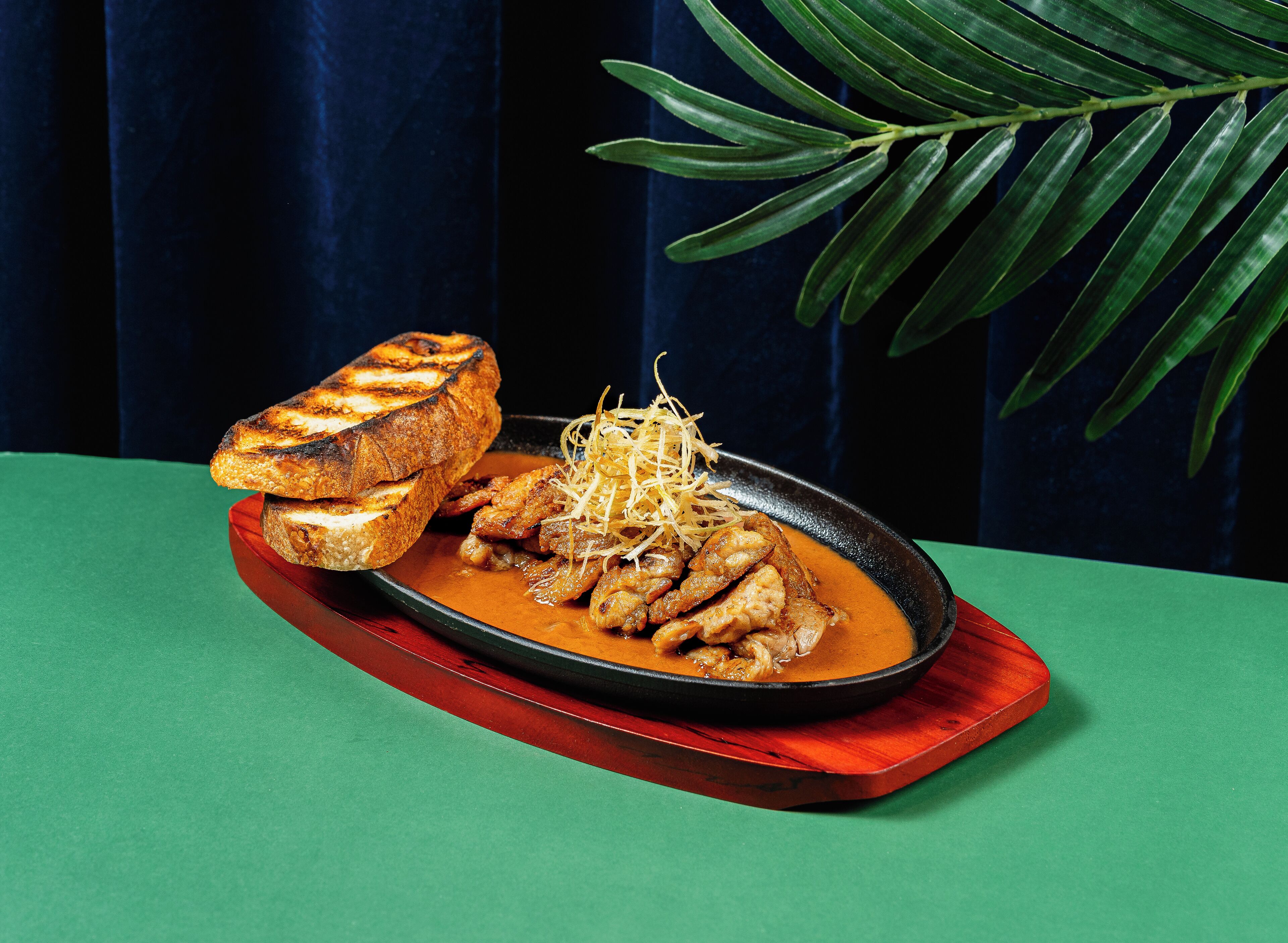 A plate of food with grilled bread and a sauce-based dish, possibly chicken, on a wooden board.