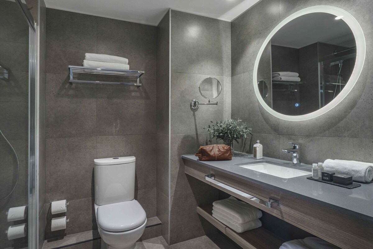 Un baño moderno con inodoro, lavamanos, espejo y zona de ducha.