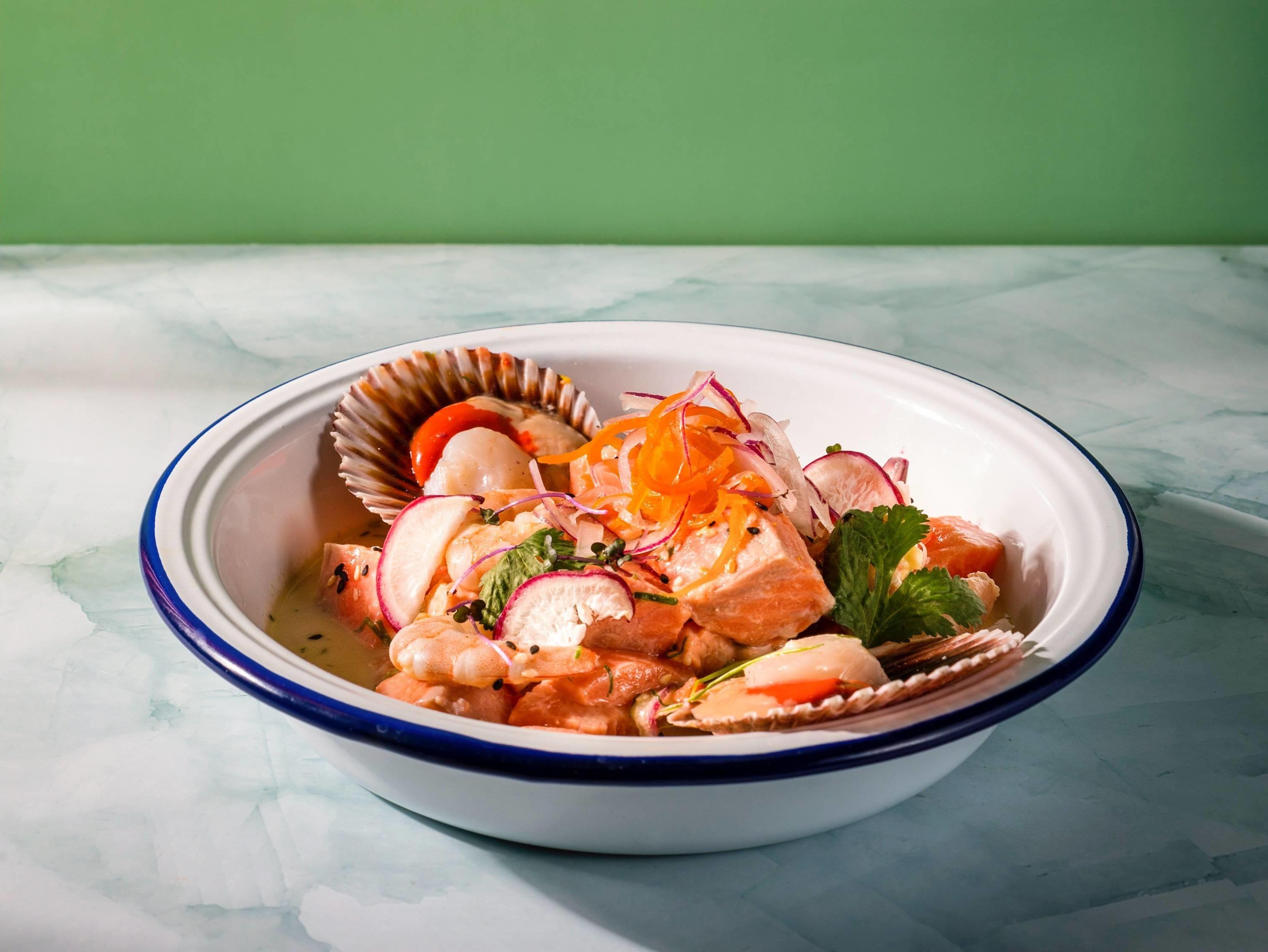Un saladier rempli de salade de fruits de mer, de radis et d’herbes aromatiques, posé sur une surface en marbre.