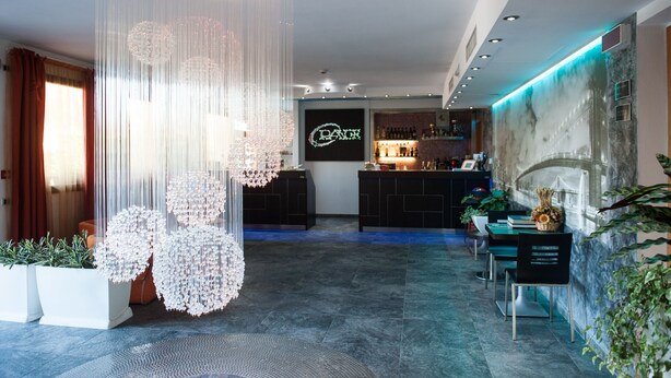 A modern bar area with a neon sign, hanging decorative lights, and a seating area with a mural.