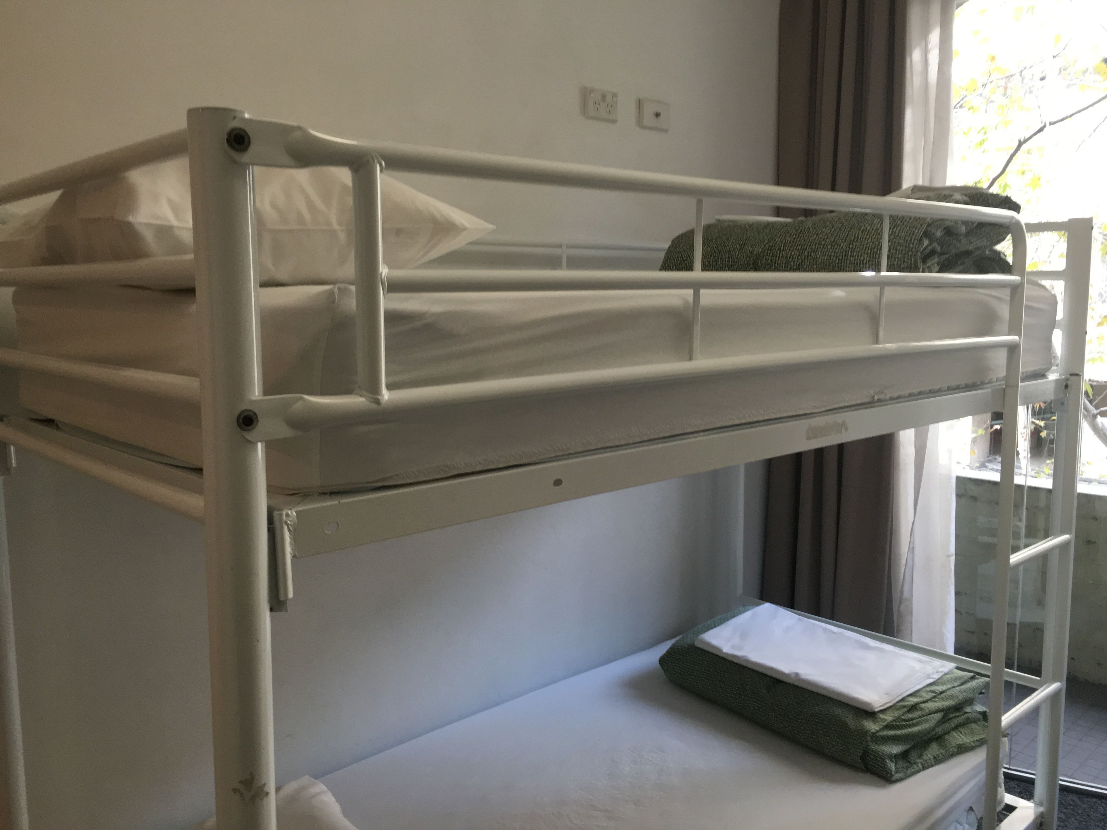 A bunk bed with a mattress and pillows, a green towel, and a window with curtains.