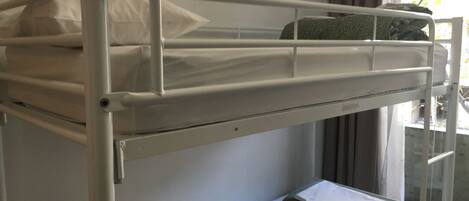 A bunk bed with a mattress and pillows, a green towel, and a window with curtains.
